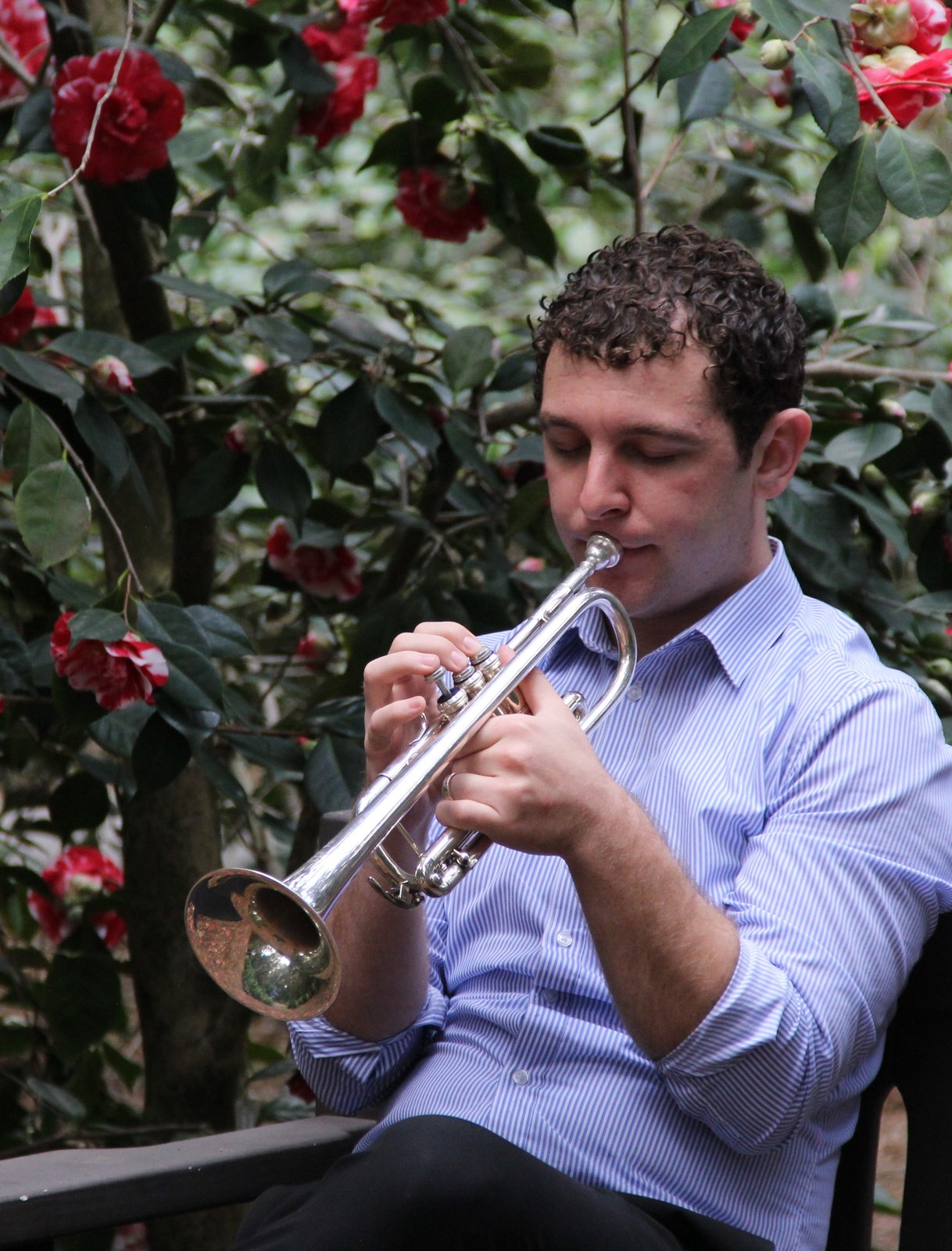 Dylan Prothro playing the trumpet, surrounded by red camellia flowers